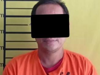 Tersangka kasus narkotika berompi tahanan berdiri di depan papan pengukuran tinggi.