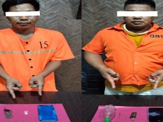 Dua tersangka kasus narkoba mengenakan baju tahanan oranye menunjukkan barang bukti sabu dan alat hisap di atas meja