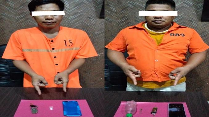 Dua tersangka kasus narkoba mengenakan baju tahanan oranye menunjukkan barang bukti sabu dan alat hisap di atas meja